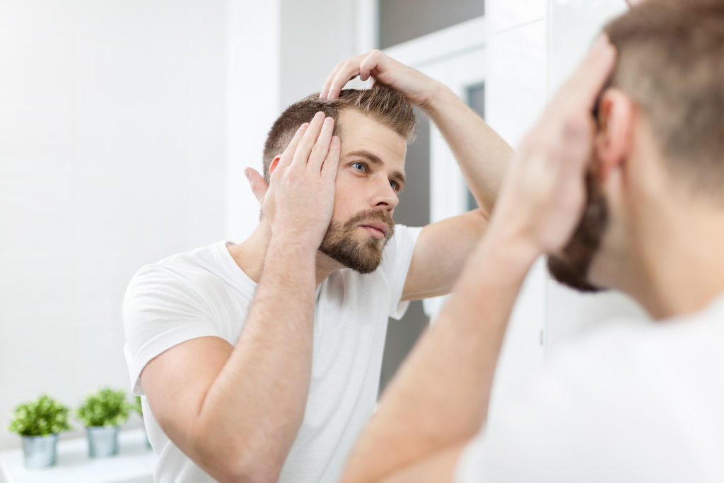 Handsome unshaven man looking into the mirror in bathroom