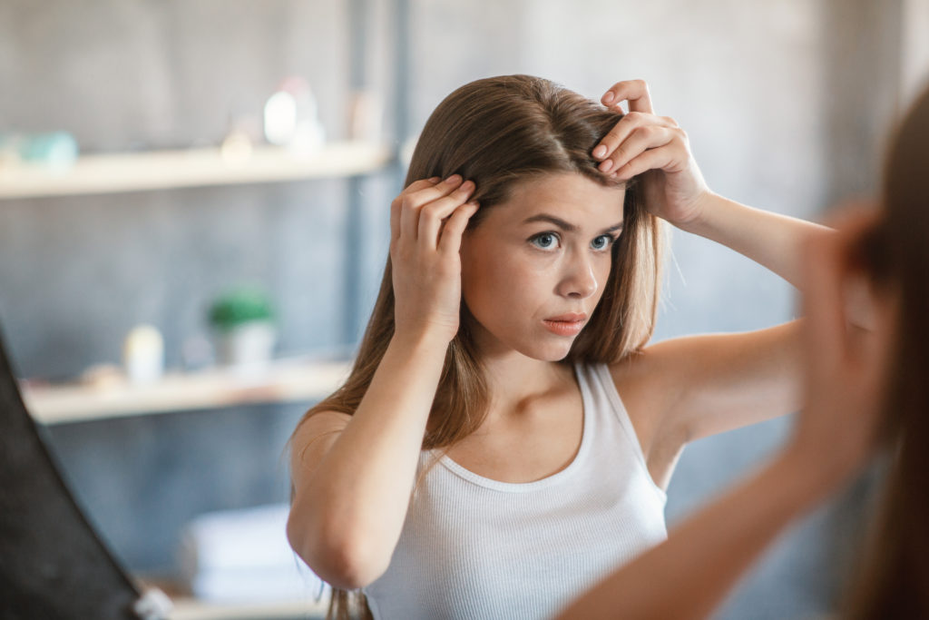 Millennial girl with hair loss problem looking in mirror at home