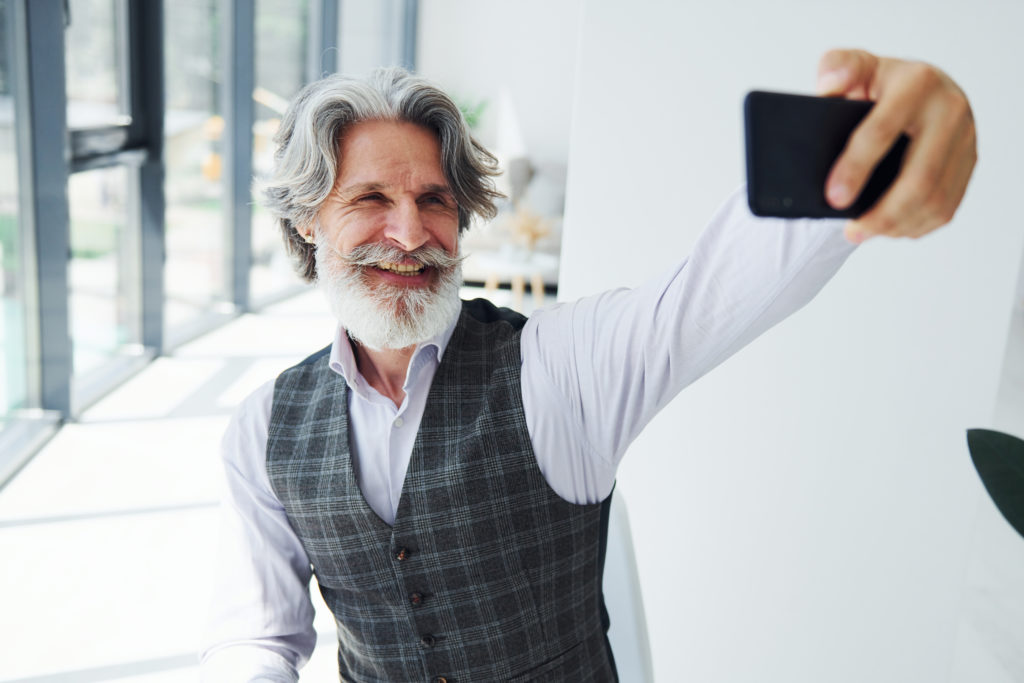 Senior stylish modern man with grey hair and beard indoors.